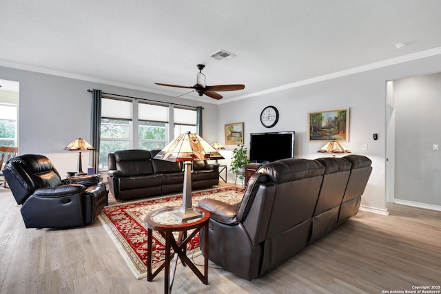 living room featuring ceiling fan, visible vents, baseboards, light wood-style floors, and ornamental molding