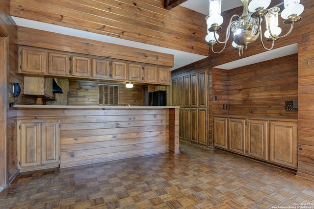 kitchen with pendant lighting, beam ceiling, wooden walls, a notable chandelier, and parquet flooring