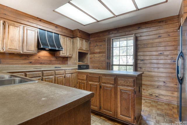 kitchen featuring parquet flooring, sink, stainless steel refrigerator, wooden walls, and range hood