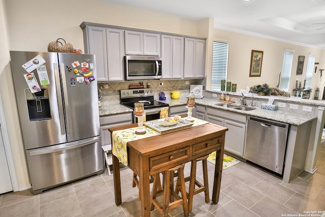 kitchen with gray cabinets, appliances with stainless steel finishes, sink, decorative backsplash, and light stone countertops