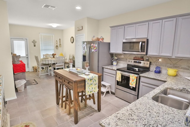 kitchen featuring stainless steel appliances, light stone countertops, and backsplash