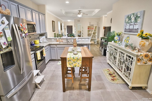 kitchen featuring appliances with stainless steel finishes, gray cabinetry, a kitchen breakfast bar, a raised ceiling, and kitchen peninsula