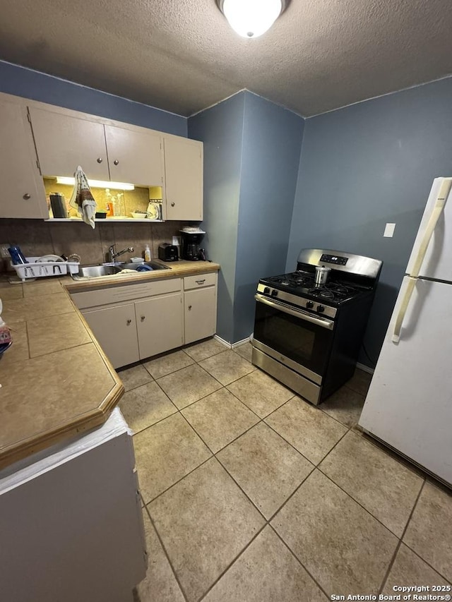 kitchen featuring gas range, white refrigerator, sink, and white cabinets