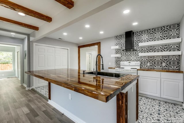 kitchen with white electric stove, sink, white cabinets, a kitchen island with sink, and wall chimney range hood