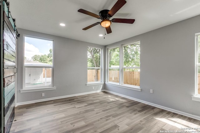 unfurnished room featuring a wealth of natural light, a barn door, ceiling fan, and light wood-type flooring