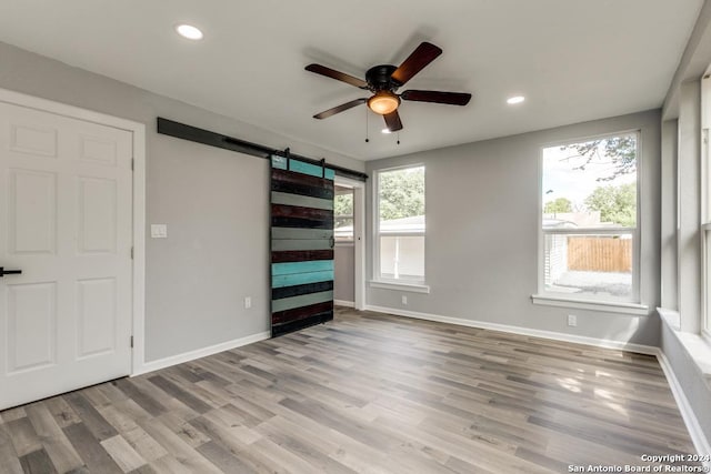 unfurnished bedroom featuring ceiling fan, a barn door, and light wood-type flooring