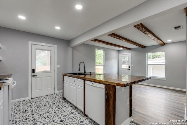 kitchen featuring sink, white appliances, white cabinetry, an island with sink, and beamed ceiling