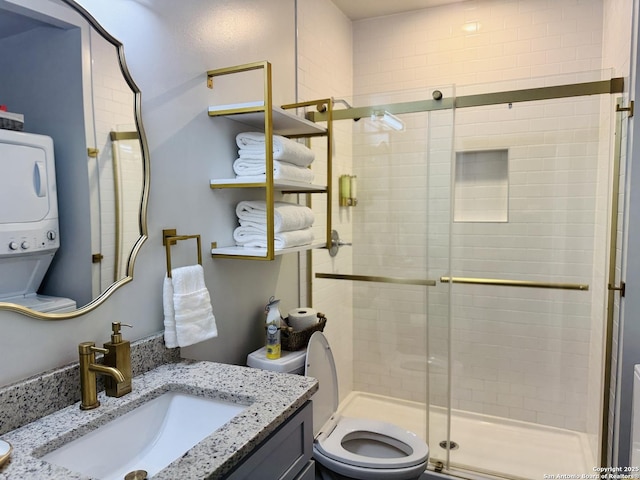 bathroom featuring vanity, stacked washer and dryer, a shower with shower door, and toilet