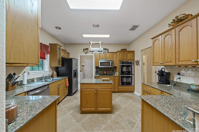 kitchen with sink, light stone counters, decorative light fixtures, appliances with stainless steel finishes, and a kitchen island