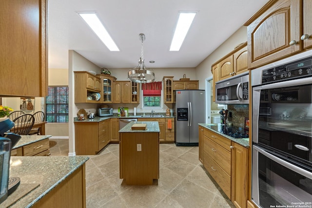 kitchen featuring sink, stainless steel appliances, light stone countertops, a kitchen island, and decorative light fixtures