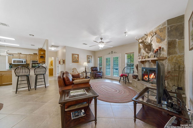 living room featuring ceiling fan, light tile patterned floors, a fireplace, and french doors