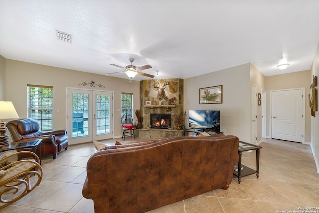 tiled living room featuring a stone fireplace, a textured ceiling, ceiling fan, and french doors