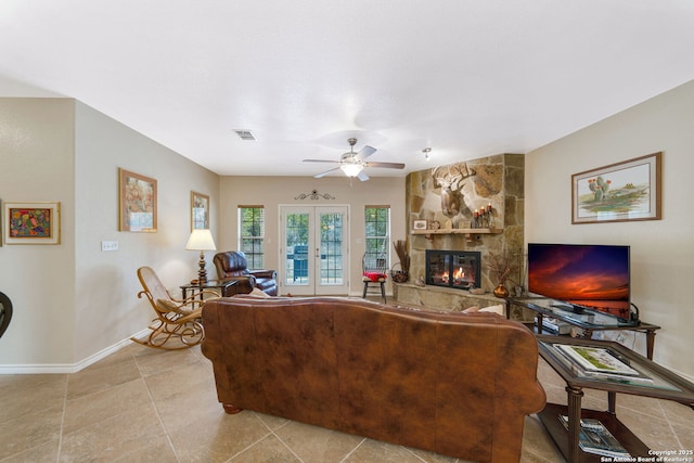 tiled living room featuring french doors, ceiling fan, and a stone fireplace