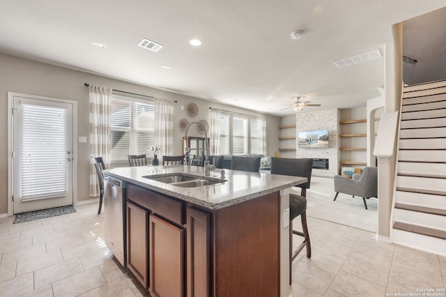 kitchen with sink, ceiling fan, dishwasher, a fireplace, and a center island with sink