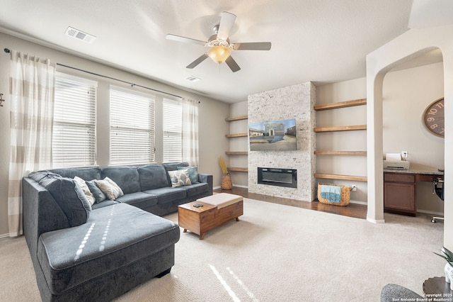 carpeted living room with a fireplace, built in features, and ceiling fan