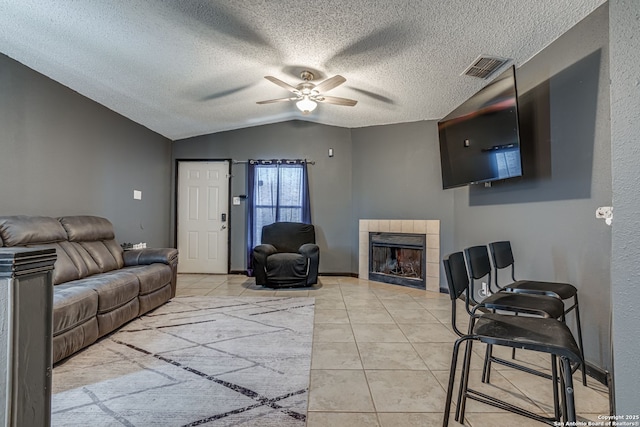 tiled living room with a tile fireplace, lofted ceiling, ceiling fan, and a textured ceiling