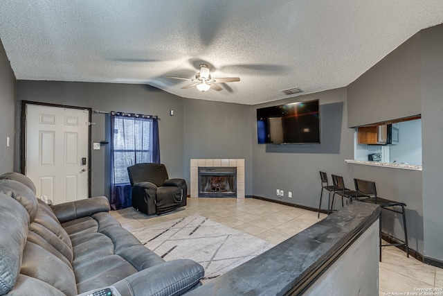 tiled living room featuring a tile fireplace, lofted ceiling, a textured ceiling, and ceiling fan