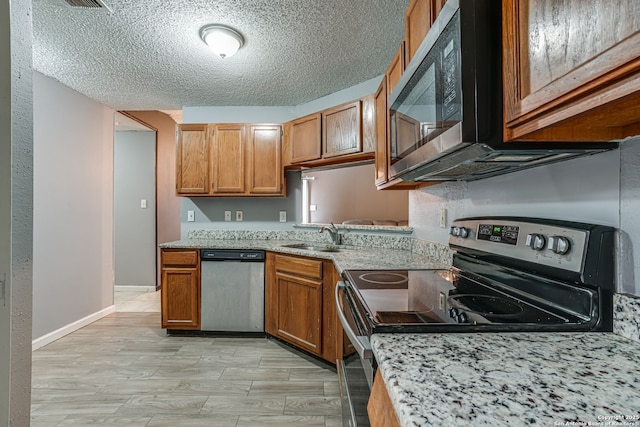 kitchen with sink, stainless steel appliances, light stone countertops, a textured ceiling, and light wood-type flooring