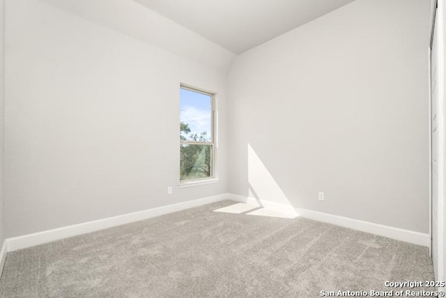 empty room with carpet floors, baseboards, and vaulted ceiling