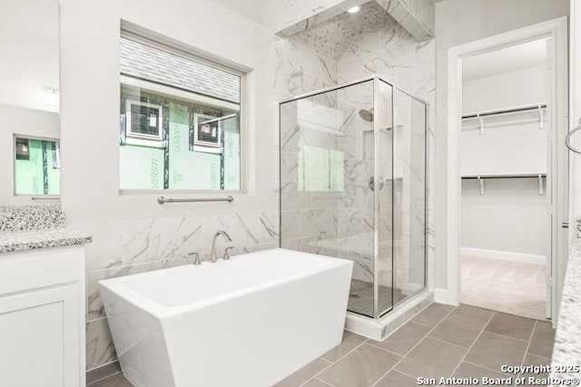 full bath with a soaking tub, a marble finish shower, a walk in closet, and vanity