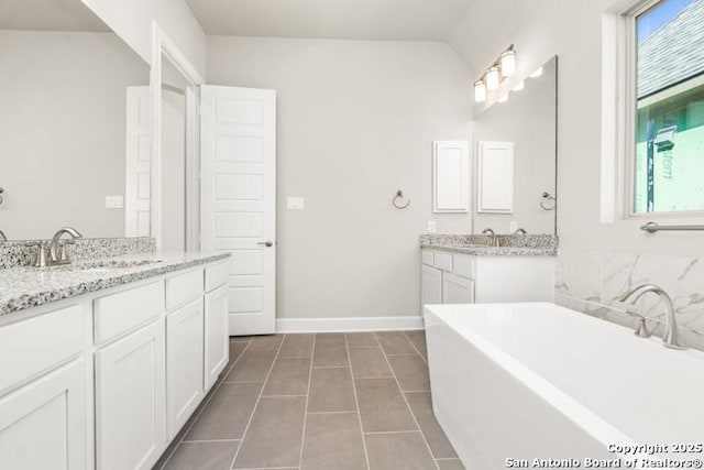 full bath featuring a wealth of natural light, a freestanding tub, two vanities, and a sink