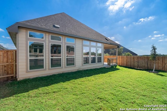 rear view of house featuring fence private yard, roof with shingles, and a lawn