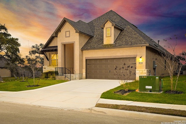 view of front facade with an attached garage, stucco siding, a shingled roof, and a yard