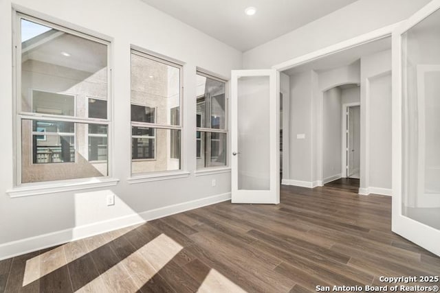 spare room with arched walkways, recessed lighting, baseboards, and wood finished floors