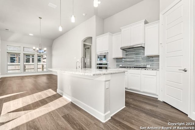 kitchen with appliances with stainless steel finishes, a kitchen island with sink, white cabinets, and decorative light fixtures