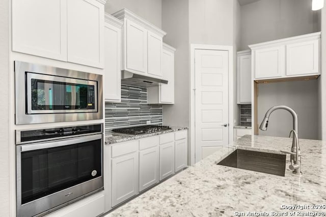 kitchen with white cabinetry, sink, decorative backsplash, stainless steel appliances, and light stone countertops