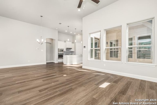 unfurnished living room featuring recessed lighting, baseboards, dark wood-type flooring, and ceiling fan with notable chandelier