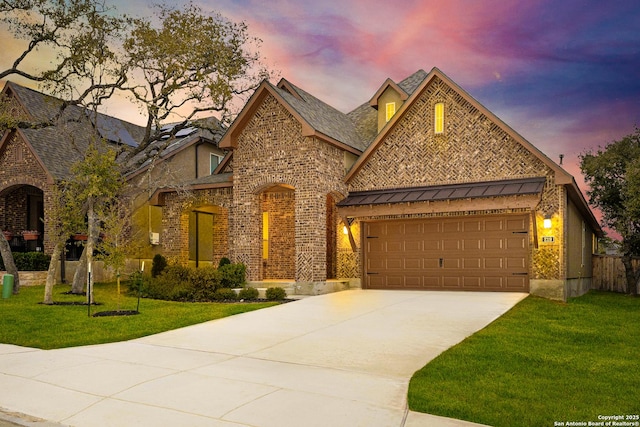 view of front of home featuring driveway, a yard, a standing seam roof, and brick siding