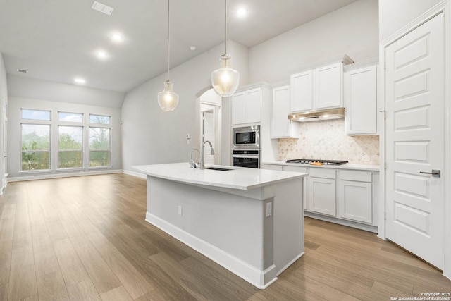 kitchen with stainless steel appliances, white cabinetry, hanging light fixtures, and a kitchen island with sink