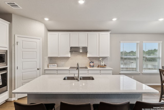 kitchen with sink, a kitchen island with sink, white cabinets, light hardwood / wood-style floors, and backsplash