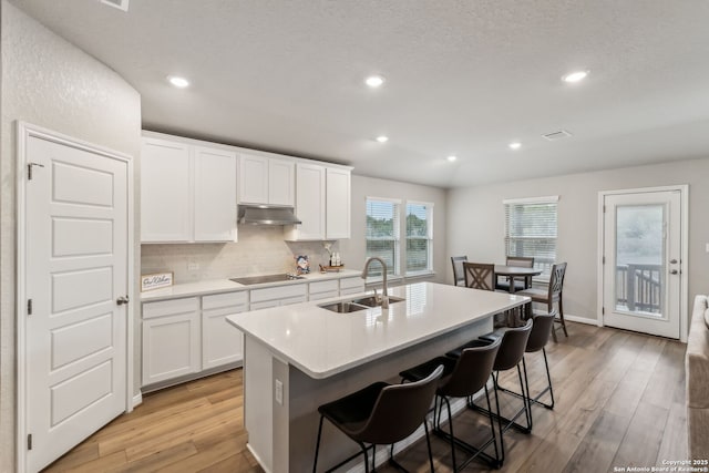 kitchen with white cabinetry, an island with sink, sink, and black electric cooktop