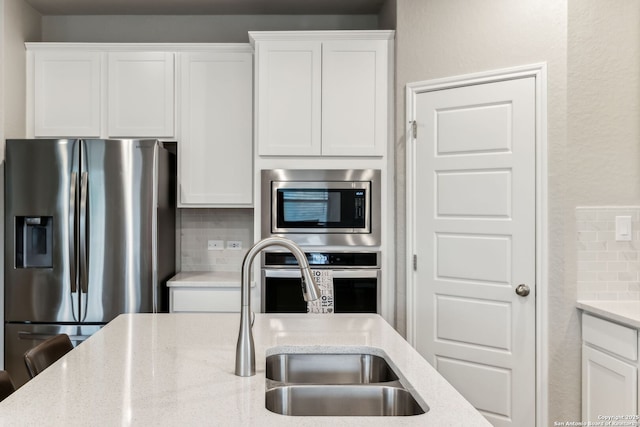 kitchen with sink, white cabinets, backsplash, stainless steel appliances, and light stone countertops