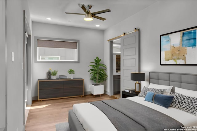 bedroom with a barn door, ceiling fan, and light hardwood / wood-style flooring