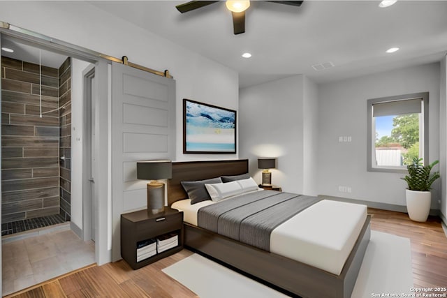 bedroom featuring ceiling fan, a barn door, and light hardwood / wood-style floors