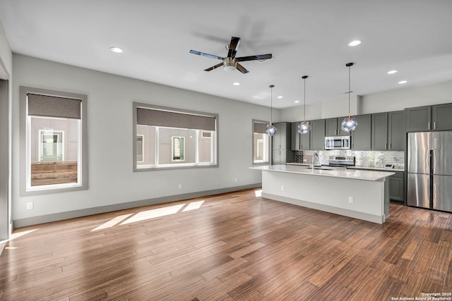 kitchen with stainless steel appliances, sink, a center island with sink, and decorative light fixtures