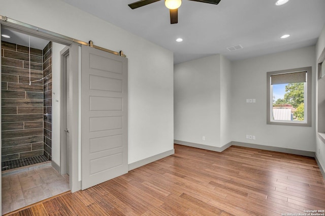 empty room with a barn door, ceiling fan, and light hardwood / wood-style flooring