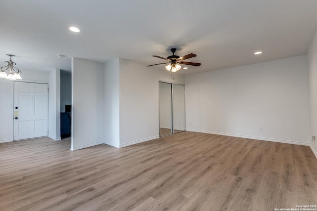 unfurnished room with ceiling fan with notable chandelier and light hardwood / wood-style floors