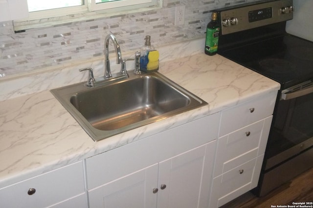 kitchen with tasteful backsplash, white cabinetry, sink, light stone counters, and electric stove