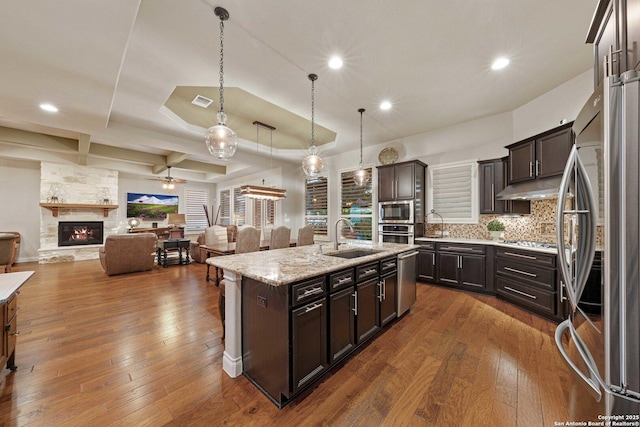 kitchen with sink, hanging light fixtures, stainless steel appliances, dark brown cabinetry, and an island with sink