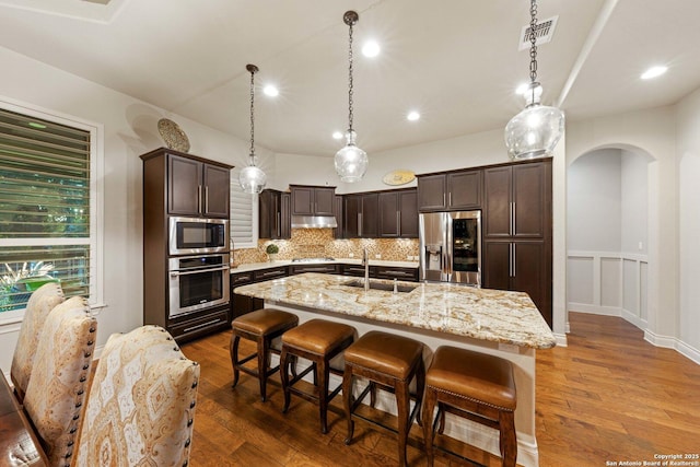 kitchen featuring appliances with stainless steel finishes, a kitchen island with sink, decorative backsplash, and decorative light fixtures