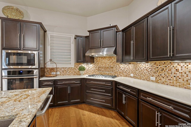 kitchen with dark brown cabinetry, appliances with stainless steel finishes, light wood-type flooring, and decorative backsplash