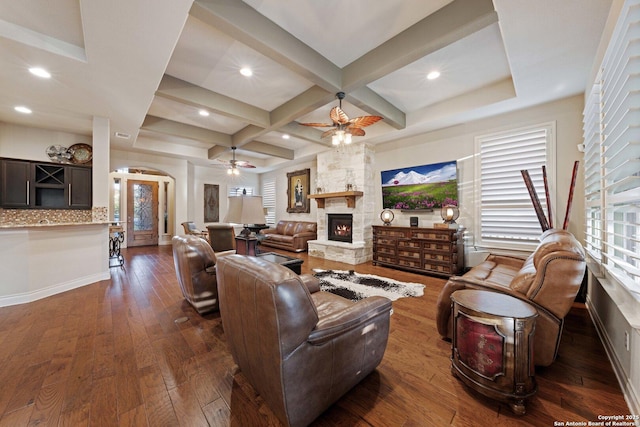 living room with dark wood-type flooring, ceiling fan, coffered ceiling, a fireplace, and beamed ceiling