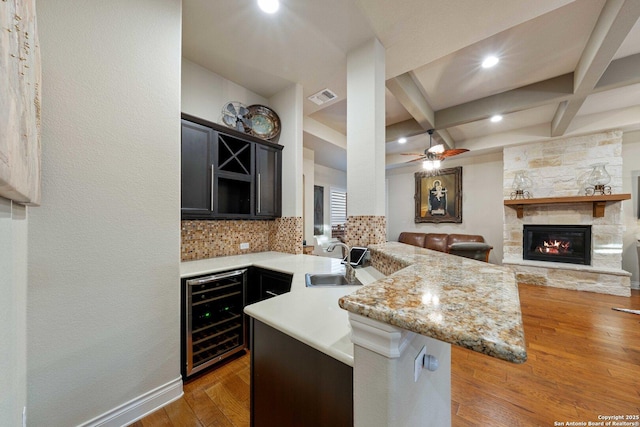 kitchen with dark hardwood / wood-style floors, coffered ceiling, light stone countertops, kitchen peninsula, and beverage cooler