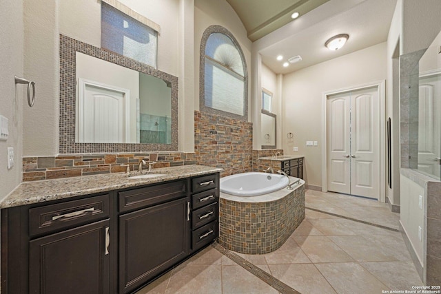 bathroom with tiled tub, vanity, vaulted ceiling, and tile patterned flooring