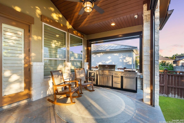 patio terrace at dusk featuring ceiling fan, grilling area, and exterior kitchen