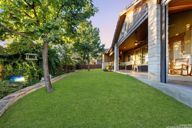 yard at dusk with ceiling fan and a patio area